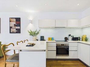 A modern kitchen with white cabinets, a built-in oven, and a dining area with a table and chairs. - Chic Baker Street Apartment with Balcony (Greater London)