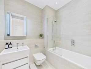 A modern bathroom with a white sink, toilet, and bathtub. - Chic Baker Street Apartment with Balcony (Greater London)