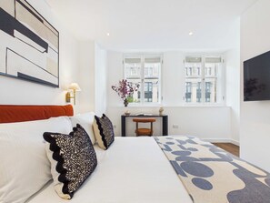 Habitació d'hotel amb un llit, una tauleta de nit, una làmpada, una finestra que mostra edifici i un quadre a la paret.
