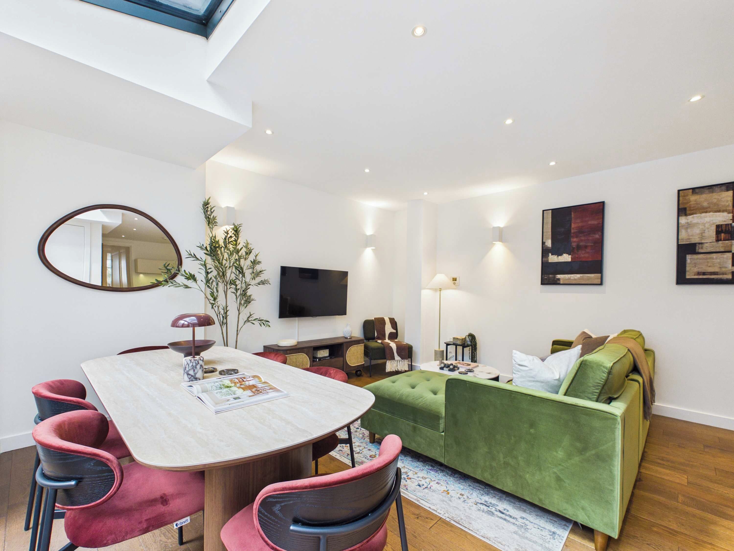 A modern living room with a dining table, chairs, a green sofa, a flat-screen TV, and artwork on the walls.
