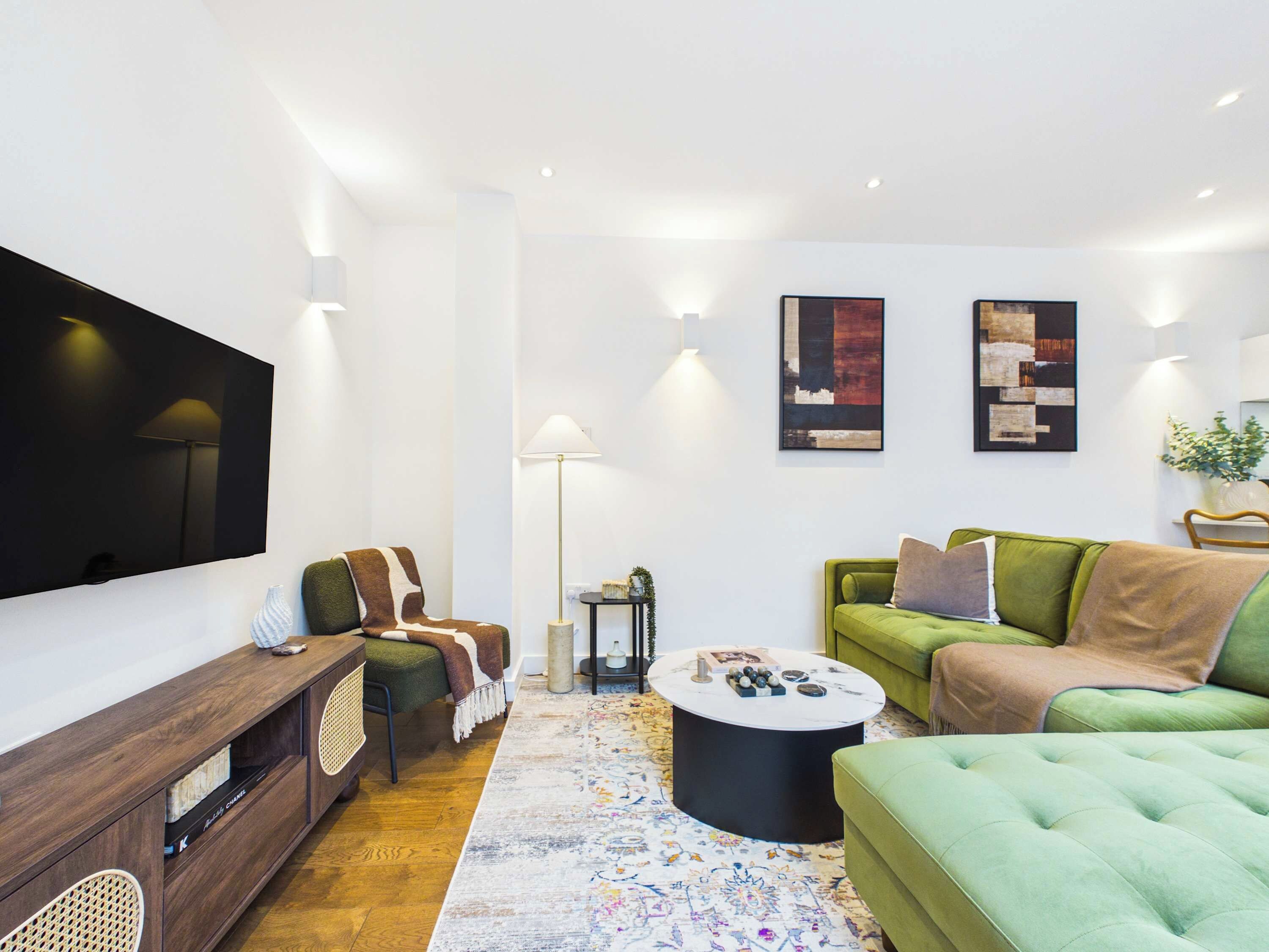 Uma sala de estar moderna com televisão de tela plana, sofá verde, tapete estampado e obras de arte nas paredes.