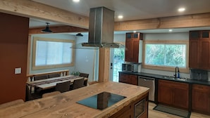 A modern kitchen with wooden cabinets, a central island with a stovetop, and a dining area with a table and chairs.