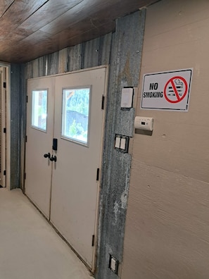 A hallway with two doors, a no-smoking sign, and a smoke detector. - Bralorne Suites & Rooms (Bralorne B.C.)