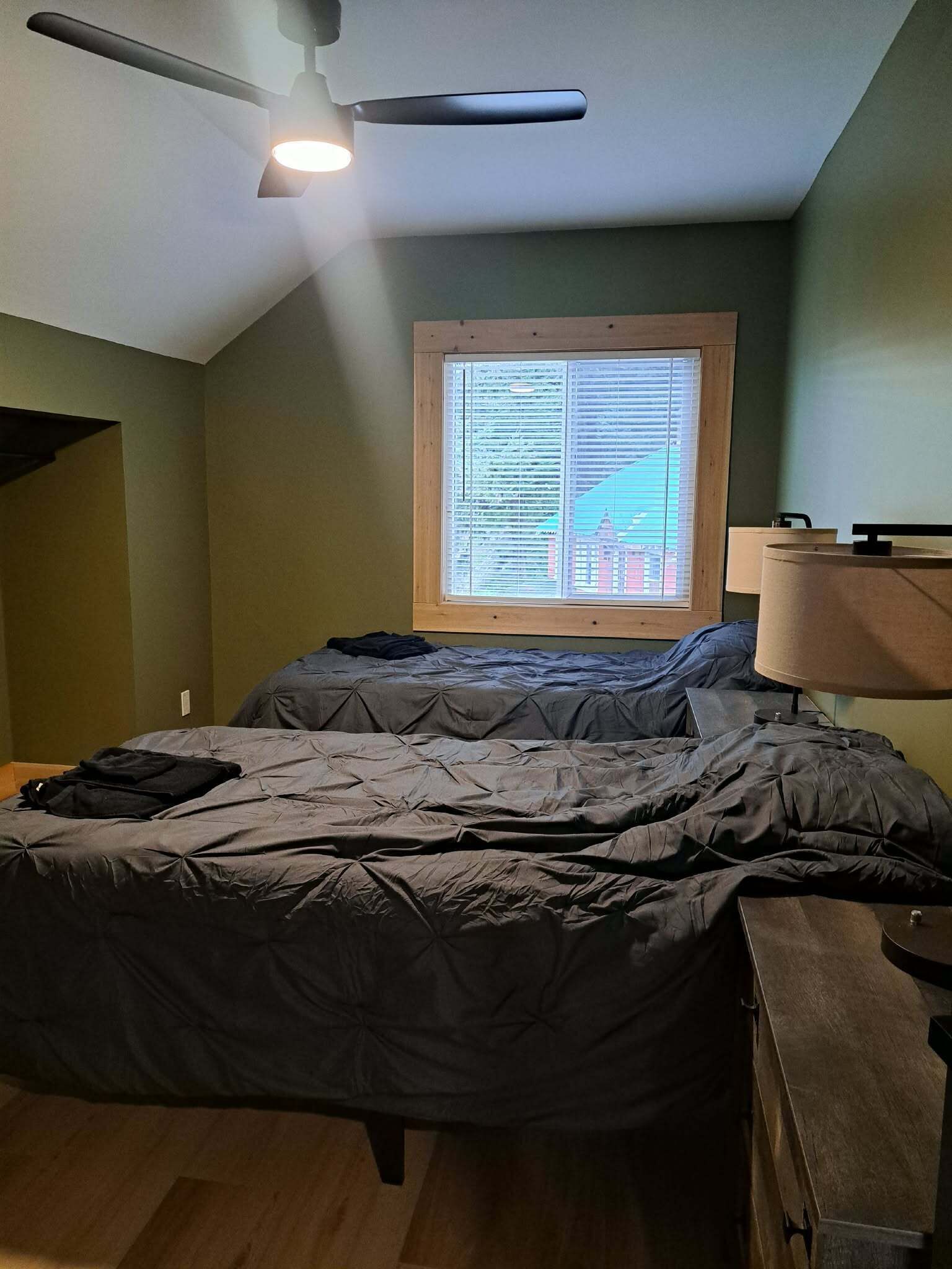 Un dormitorio con cama, ventana con persianas, ventilador de techo y lámpara.