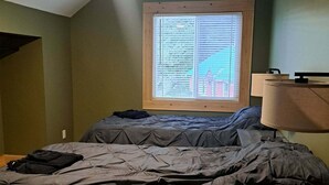 A bedroom with a bed, a window with blinds, a ceiling fan, and a lamp.