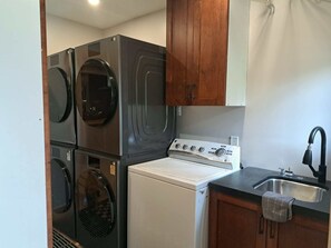 A compact kitchen with a built-in washer and dryer, a stove, and a sink. - Bralorne Suites & Rooms (Bralorne B.C.)