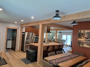 A modern kitchen with stainless steel appliances, a wooden dining area with a patterned runner, and a large window. - Bralorne Suites & Rooms (Bralorne B.C.)