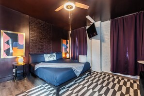 Ein modernes Schlafzimmer mit einem Bett, einem Deckenventilator, einer Ziegelwand, einem an der Wand montierten Fernseher und einem gemusterten Teppich.