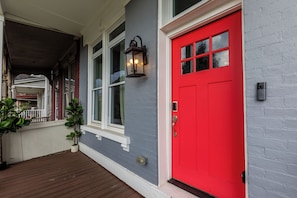 Ein Haus mit roter Tür, einer Veranda mit Holzboden und einem Blumentopf.