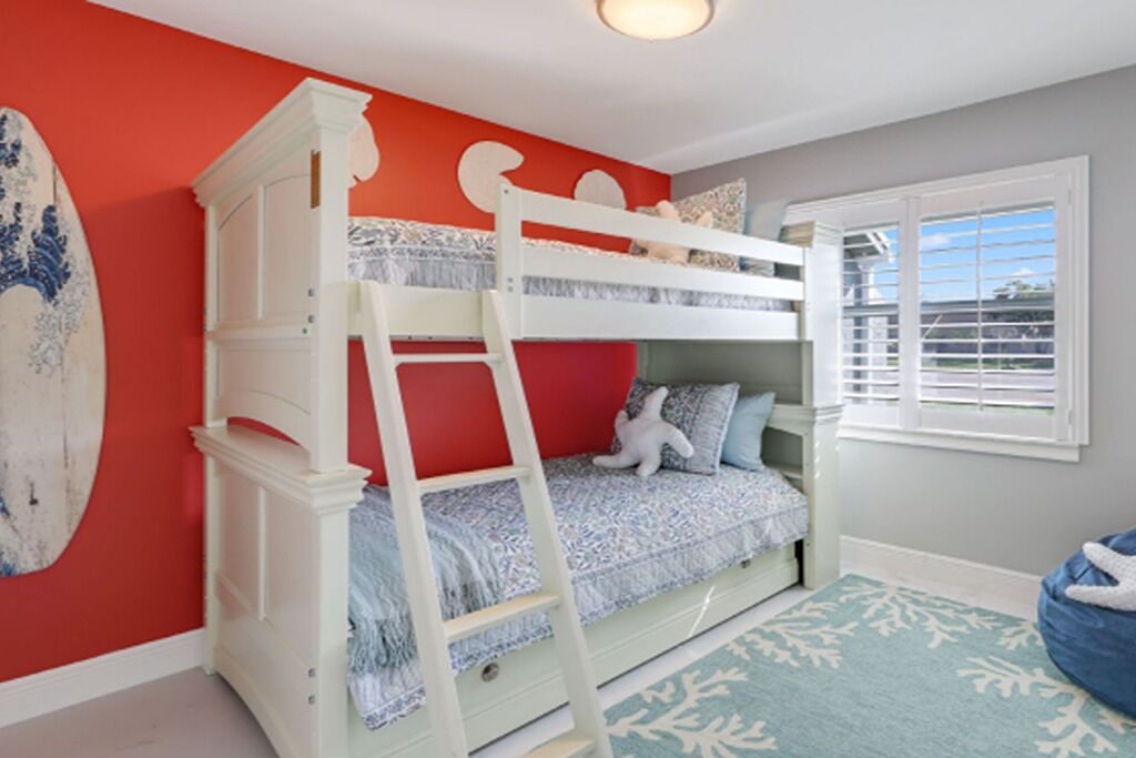 A bunk bed with a ladder, a surfboard, and a window with blinds.