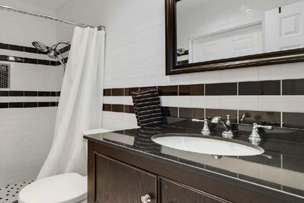 Ein Badezimmer mit einer weißen Toilette, einem schwarzen Waschtisch mit Spiegel und einer Duschvorhang.