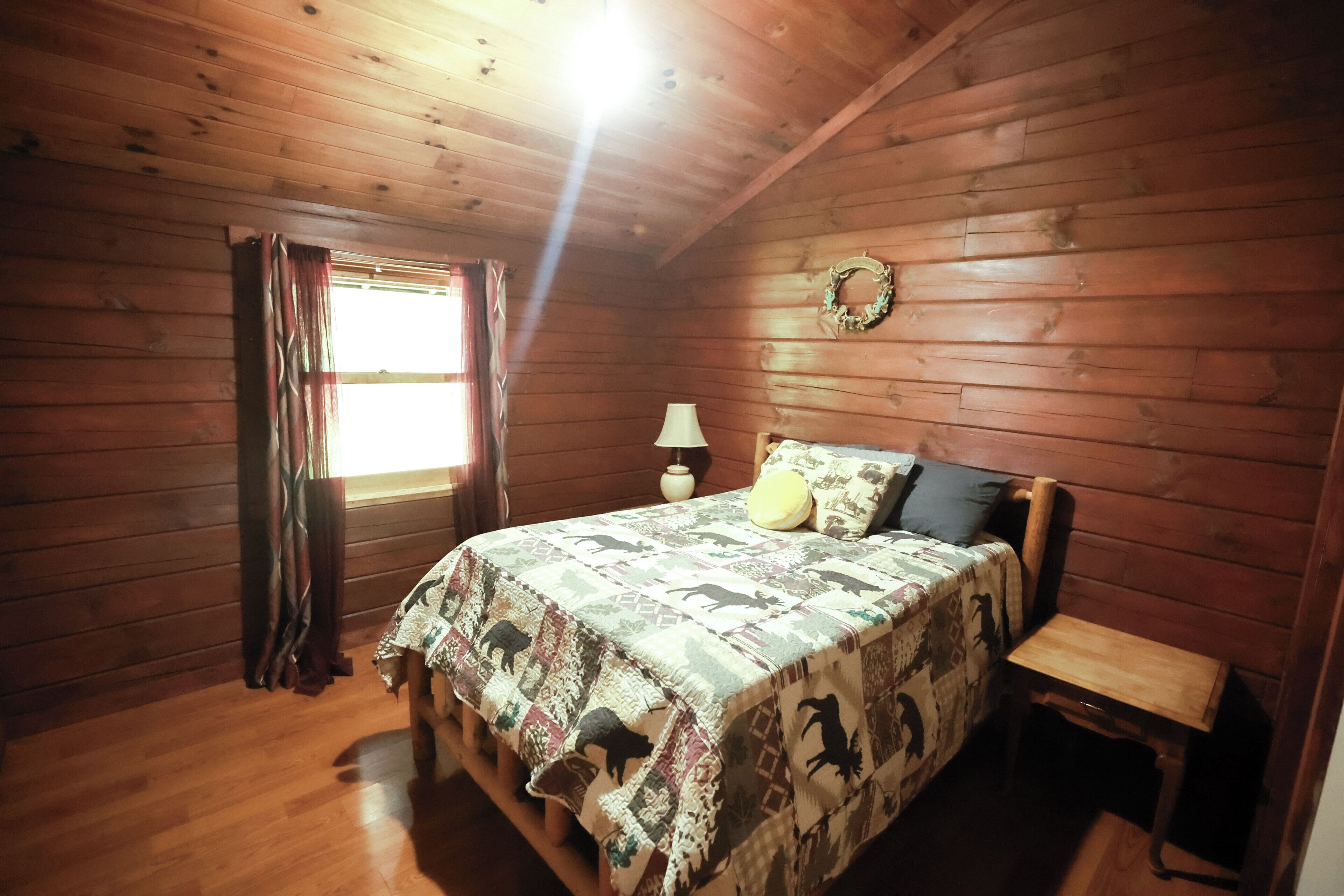 Une chambre à coucher aux murs lambrissés, avec un lit, une table de chevet, une lampe et une fenêtre avec des rideaux.