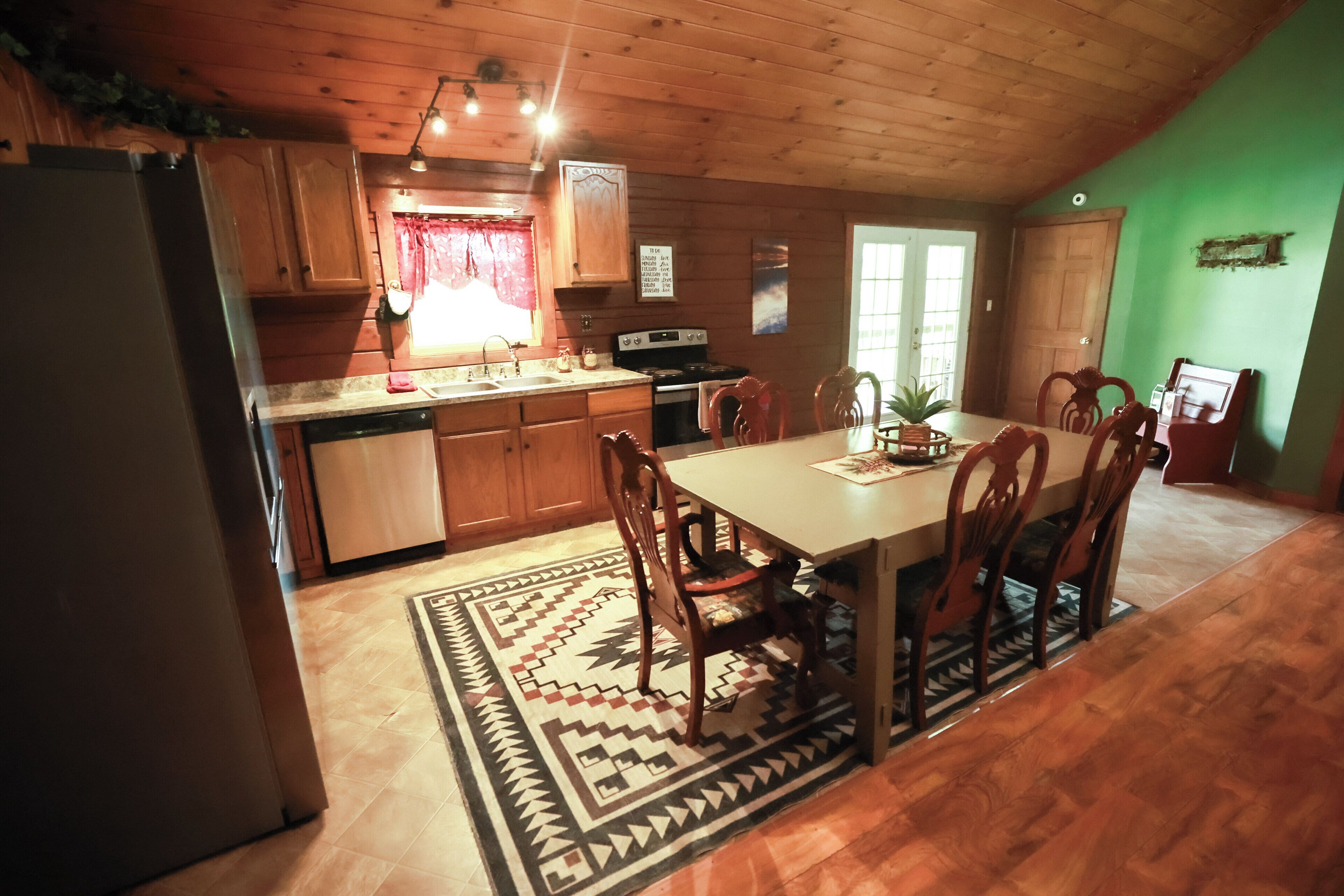 A kitchen with wooden cabinets, a dining table with chairs, a refrigerator, and a patterned rug.