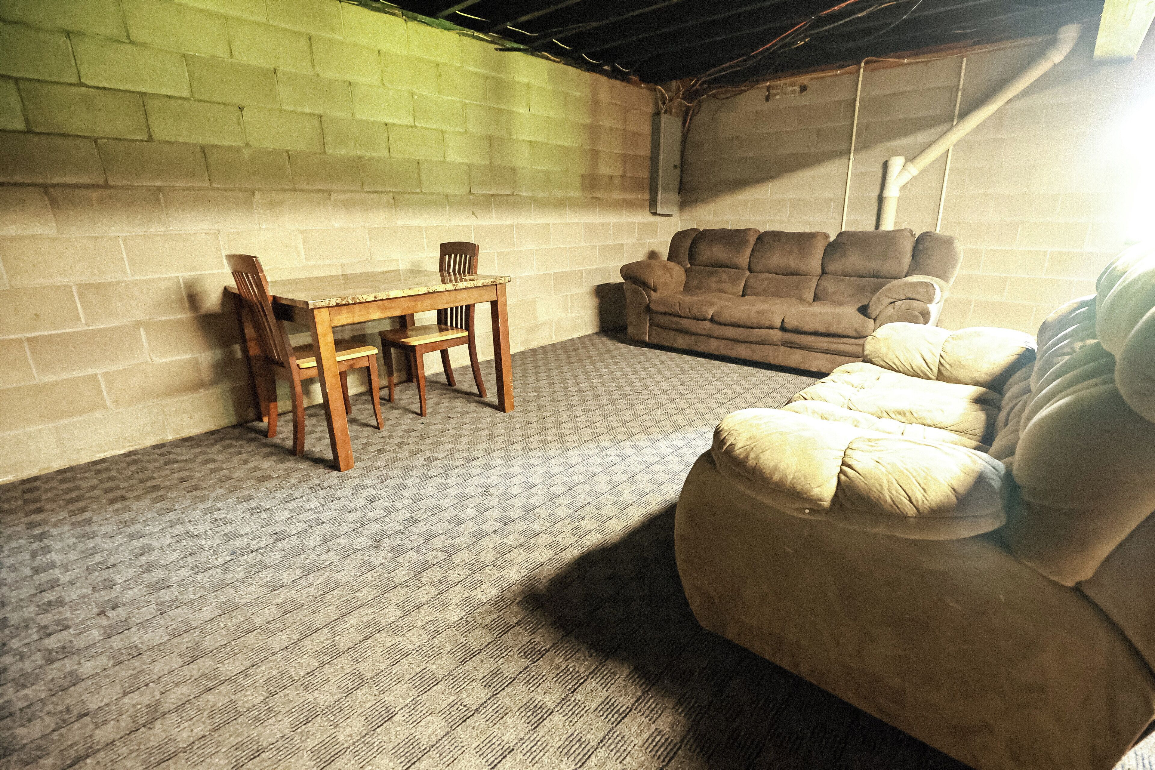 Una habitación con pared de ladrillo, una mesa de madera con sillas, un sofá marrón y una alfombra estampada.