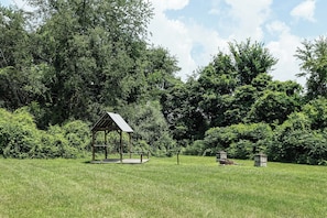 A gazebo in a grassy field with dense trees in the background.