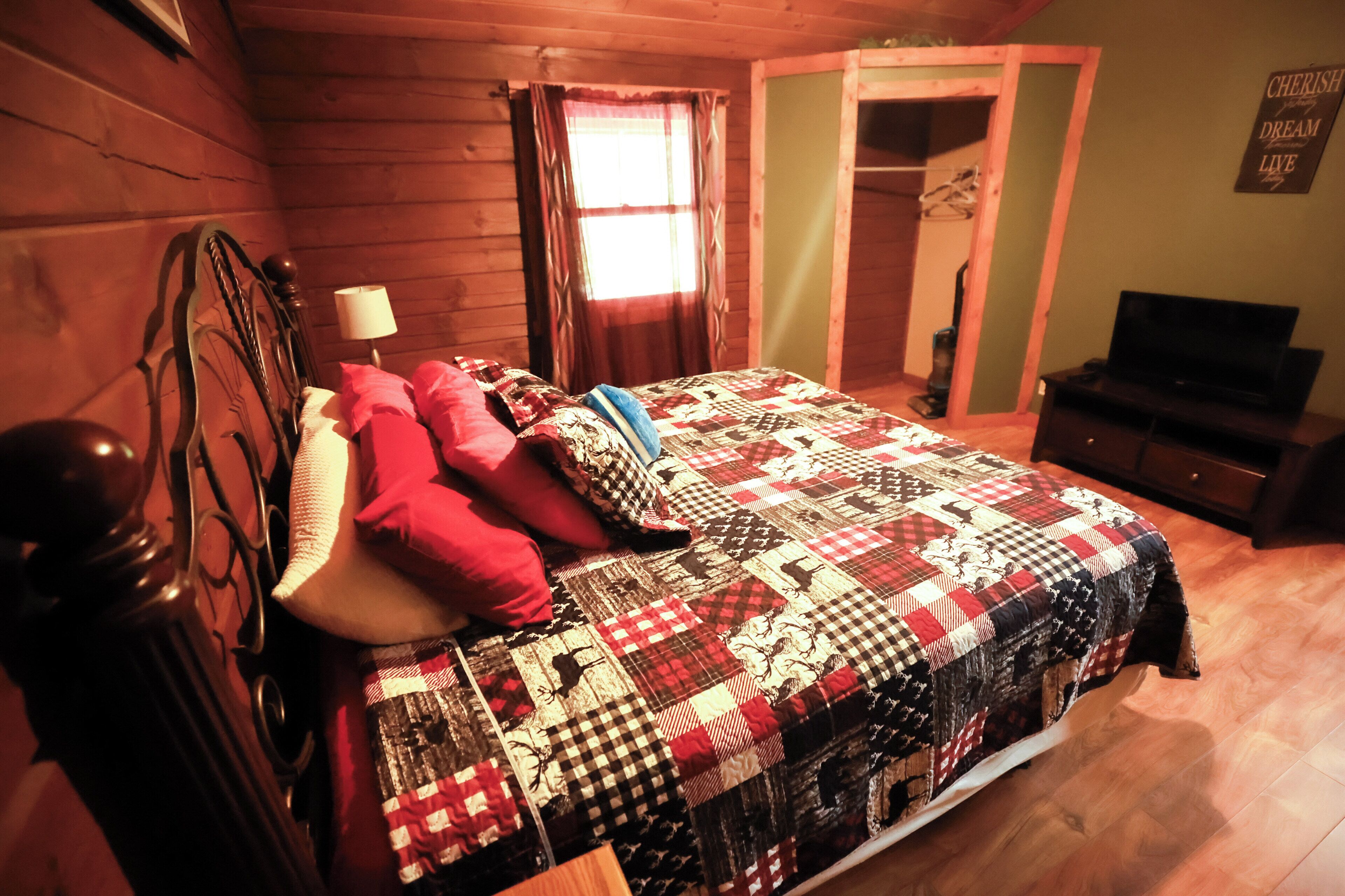 A bedroom with a wooden headboard, a quilted bedspread, a television, and a door leading to another room.