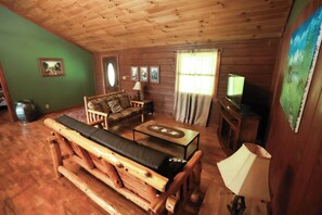 A wooden cabin interior with a sofa, a table, a television, and a fireplace.