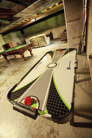 A billiards table with a cue stick and balls, a pool table in the background, and a brick wall.