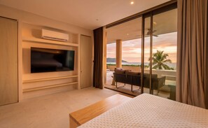 A modern hotel room with a flat-screen TV, a bed, a balcony with a view of the sea, and a ceiling fan. - Anera Apt with Plunge Pool Overlooking the Ocean (Playa Blanca)