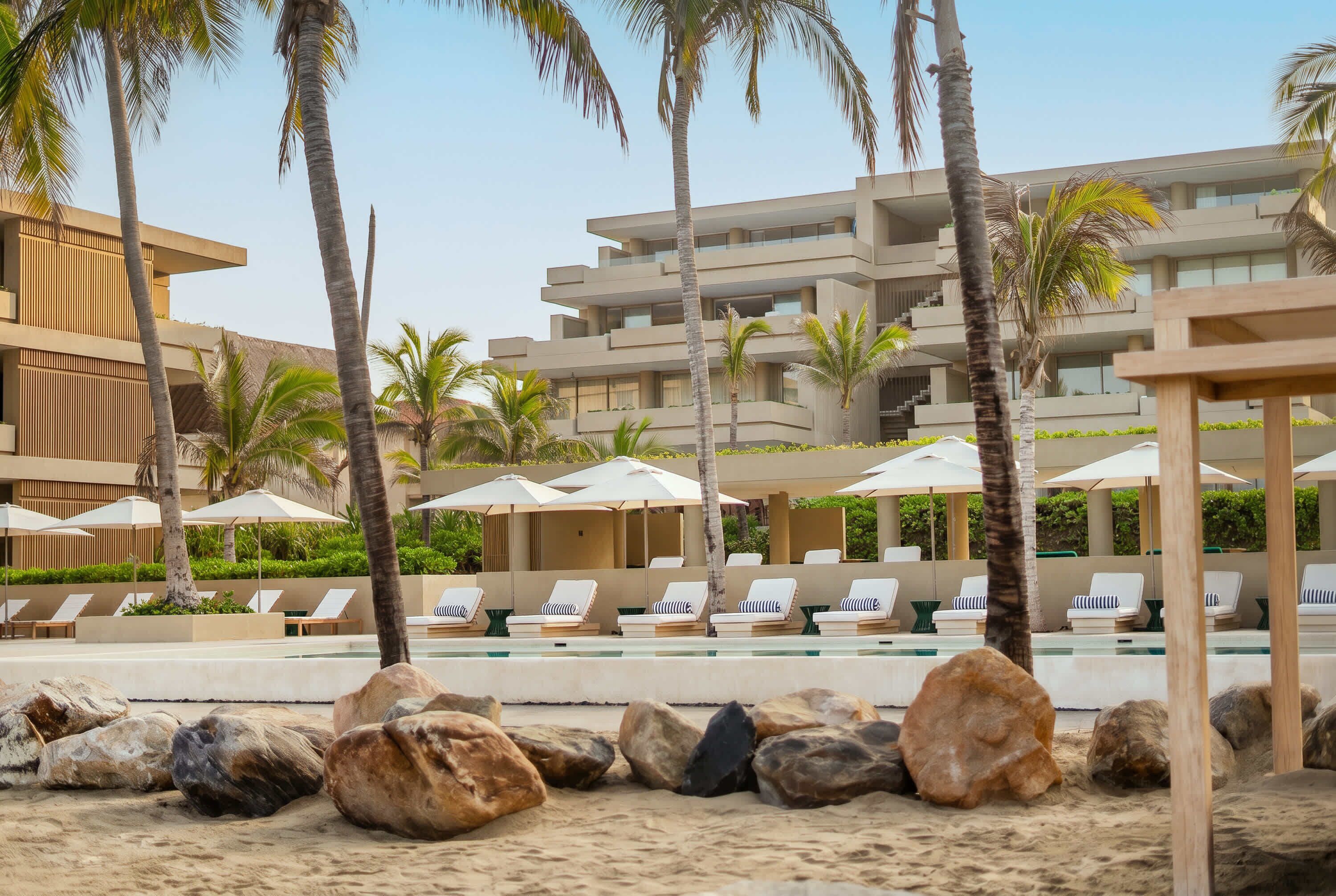 A resort with a pool area, lounge chairs, palm trees, and a modern building.
