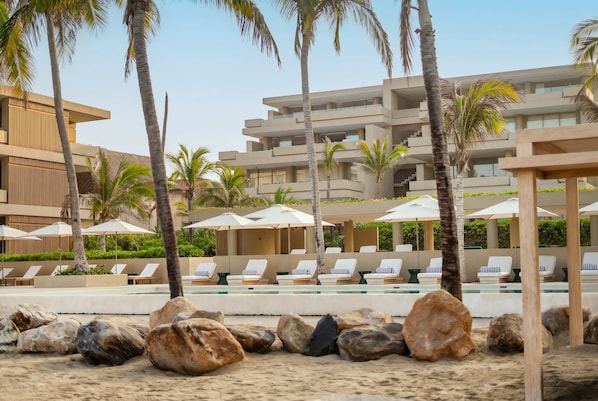 A resort with a pool area, lounge chairs, palm trees, and a modern building.