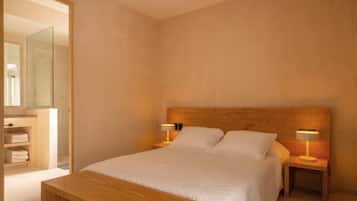A bedroom with a wooden headboard, two bedside lamps, a bed with white linens, a wooden nightstand, and a wooden bench.