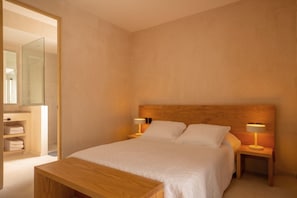 A bedroom with a wooden headboard, two bedside lamps, a bed with white linens, a wooden nightstand, and a wooden bench.