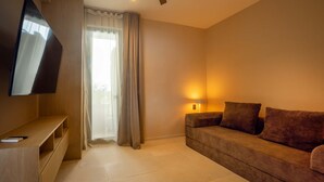Ein Hotelzimmer mit einem an der Wand befestigten Flachbildfernseher, einer Couch mit Kissen, einer Nachttischlampe und einem Fenster mit Vorhängen.
