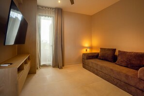 A hotel room with a flat-screen TV mounted on the wall, a sofa with cushions, a bedside lamp, and a window with curtains. - Anera Apt with Plunge Pool Overlooking the Ocean (Playa Blanca)