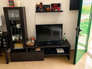 Ein Zimmer mit Fernseher, einem Schrank mit Glastüren, einem Regal mit Dekorationen und einer grünen Tür.