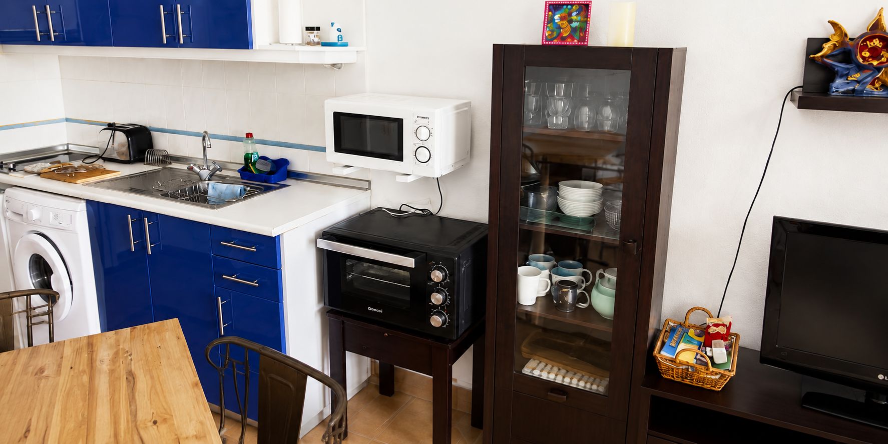 Eine kompakte Küche mit Mikrowelle, Toaster und Backofen, einer Waschmaschine sowie einem Essbereich mit Tisch und Stühlen.