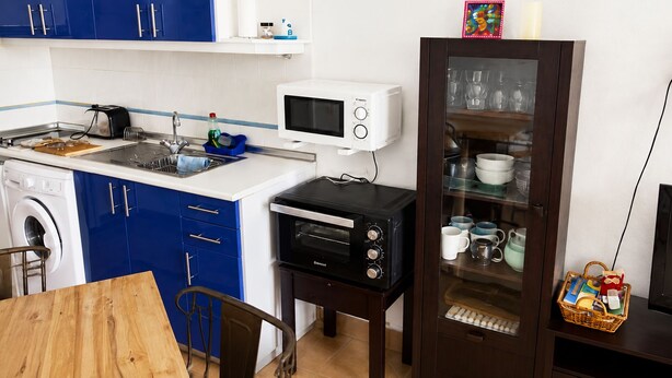 Cozinha compacta equipada com micro-ondas, torradeira e forno, além de máquina de lavar e área de jantar com mesa e cadeiras.