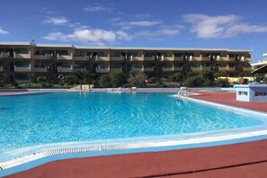 A swimming pool with a red deck, surrounded by a multi-story building with balconies. - Bouganville Sea & Pool View Brigit Apartment—perfectly laid out for your comfort. (Nuevo Horizonte)