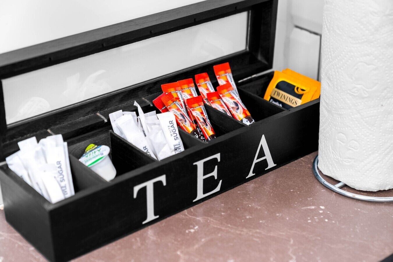 Eine schwarze Box mit Fächern, die mit 'TEE' beschriftet sind, mit verschiedenen Teebeuteln und einer gelben Box mit der Aufschrift 'TWINKING'.