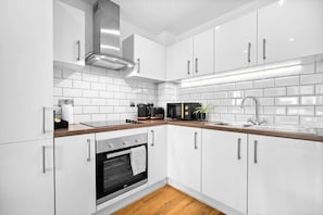 Una cucina moderna con mobili bianchi, una cappa aspirante in acciaio inossidabile, un forno integrato e un piano di lavoro con macchina da caffè e tostapane.
