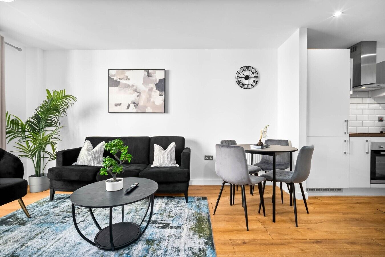 A modern living room with a black sofa, a round coffee table, and a dining area with grey chairs.