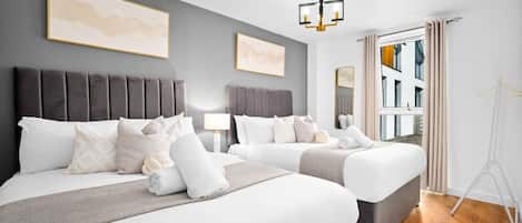 A hotel room with two beds, a grey headboard, a hanging light fixture, and a window with curtains.