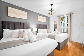 A hotel room with two beds, a grey headboard, a hanging light fixture, and a window with curtains. - City Centre Apartment* 4 Guests* Jewellery Quarter (West Midlands)