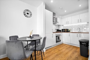 Una cucina moderna con mobili bianchi, una sveglia nera e un'area pranzo con sedie grigie.