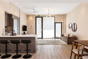 A modern kitchen with a bar area, a seating area with a sofa and chairs, and a large window providing natural light. - Waou Essence III Tétouan - Short-Term (Madrid)