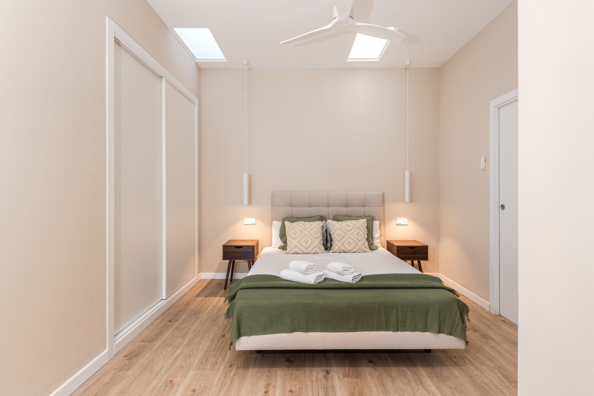 A bedroom with a bed, two bedside tables, a ceiling fan, and a skylight.