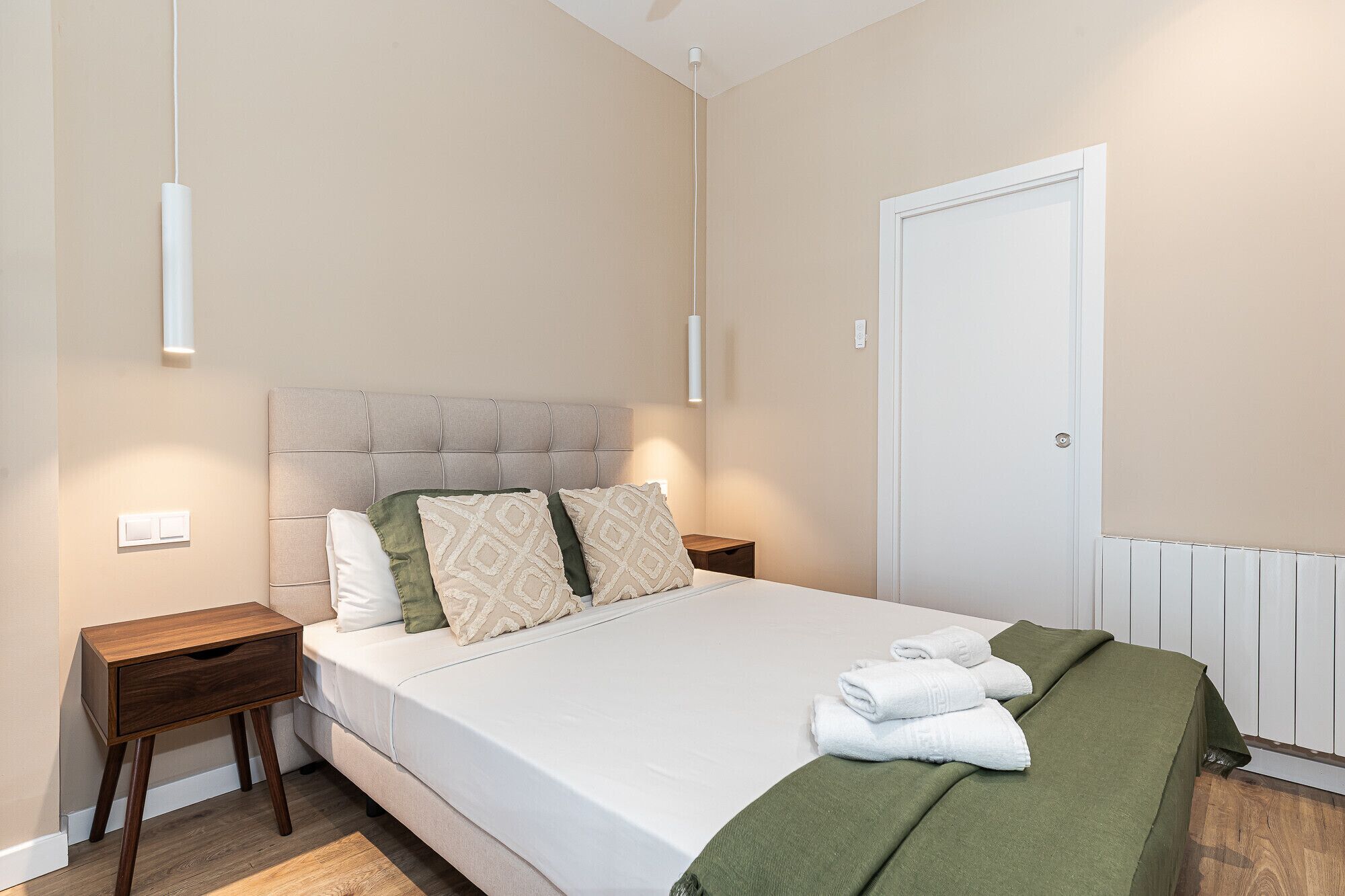 Ein Schlafzimmer mit Bett, Nachttischen, Heizkörper und Tür.