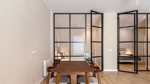 A modern interior with a dining area, a visible bed, and a bathroom in the background. - Waou Essence III Tétouan - Short-Term (Madrid)