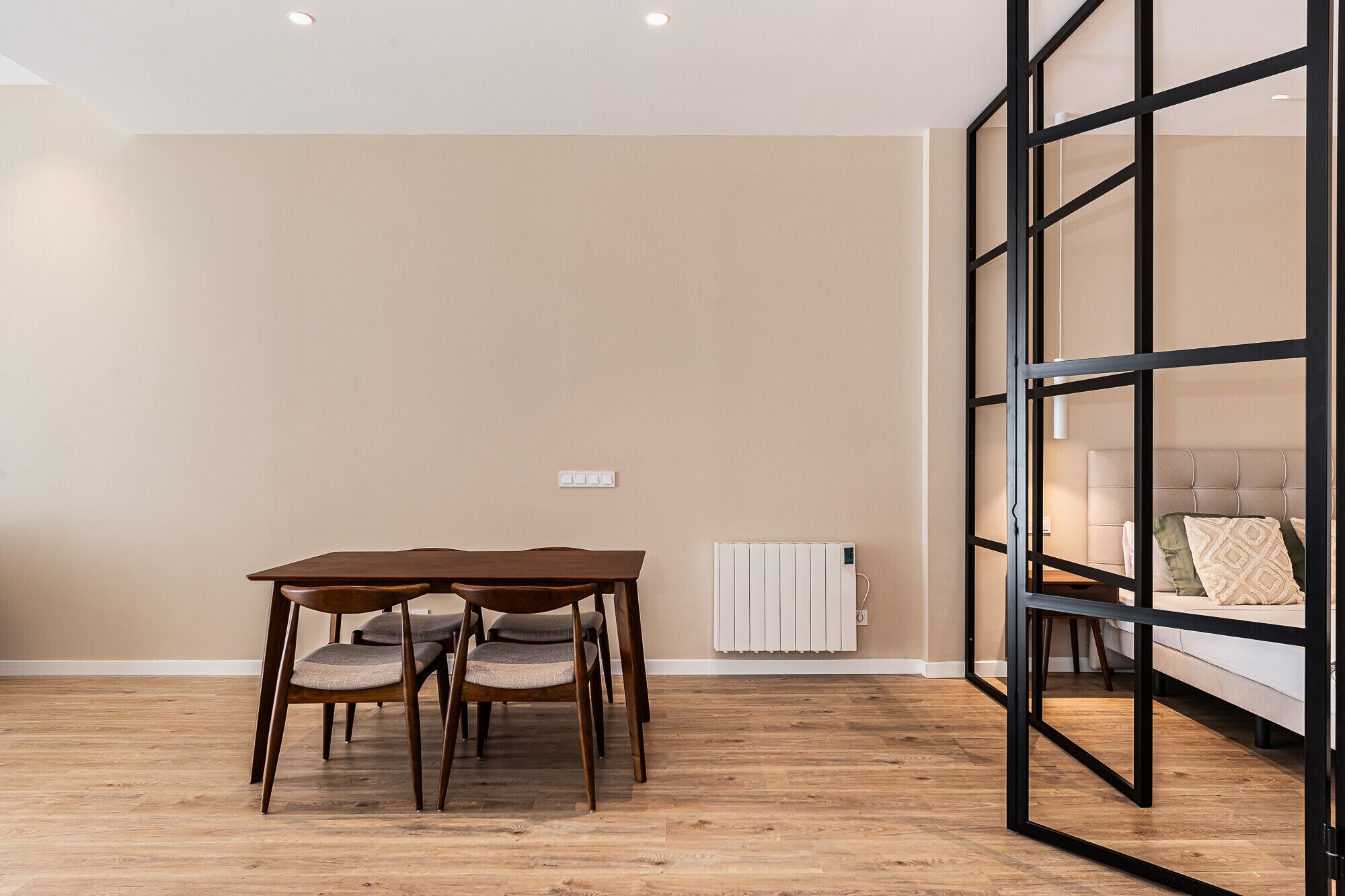 A room with a wooden table and chairs, a radiator, and a bed with a headboard.