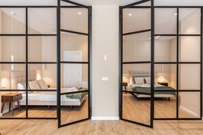 Une chambre d’hôtel dotée d’une grande porte coulissante qui sépare deux chambres, chacune comprenant un lit, une table de chevet et une lampe.