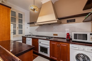 A kitchen with a built-in oven, microwave, and washing machine, wooden cabinets, and a hanging light fixture. - Waou Sol XII - Short-Term Rental (Madrid)