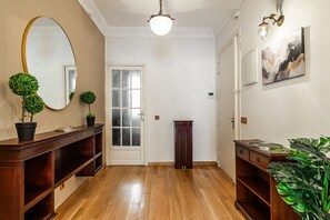 A hallway with wooden flooring, a mirror, a door, a small table, and a potted plant. - Waou Sol XII - Short-Term Rental (Madrid)