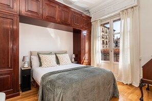 Un dormitorio con cama, armario de madera, mesitas de noche y ventana con cortinas.