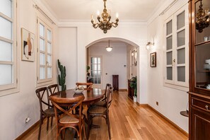 Ein Essbereich mit Holztisch und Stühlen, einer Chandelierleuchtre und Blick in einen anderen Raum durch einen Rundbogen.