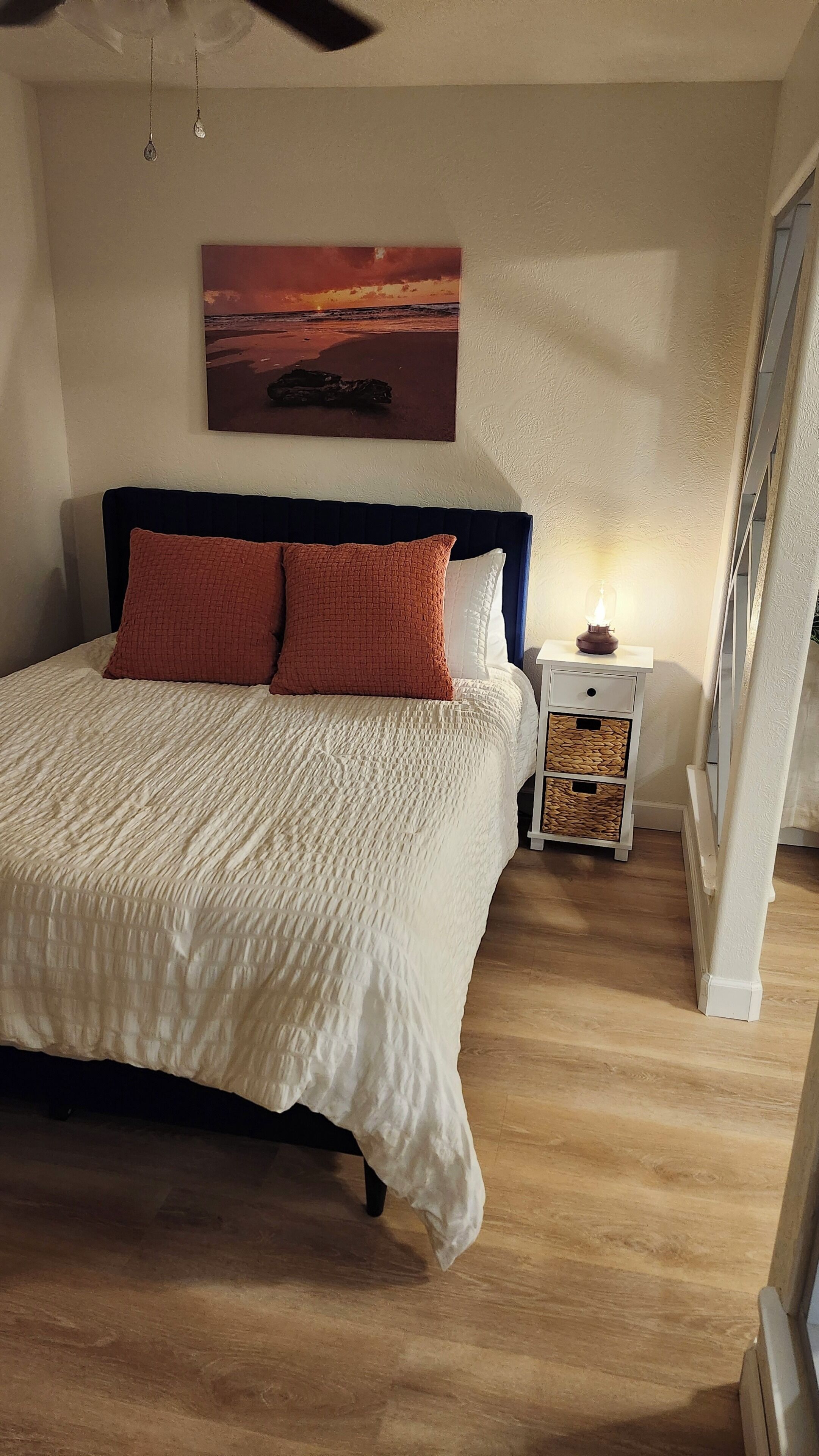 Une chambre à coucher avec un lit, une table de chevet, une lampe, un tableau au mur et une fenêtre.